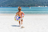 Rear view of carefree kid running with swimming tube towards sea.