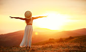 Happy woman standing with her back on sunset in nature iwith open hands