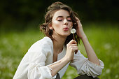 Spring portrait of a girl sitting in a field on the grass among dandelion flowers. Cheerful girl enjoys Sunny spring weather. Natural beauty of a woman, natural cosmetics