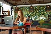 Beautiful millennial woman typing on laptop sitting at table in bohemian cafe in Bali Indonesia