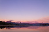 Beautiful Patagonia landscape of Andes mountain range with high mountains with illuminated peaks, stones in mountain lake, reflection, violet sky and fog at the sunset.