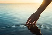 Happy people in nature. A woman feeling and touching the ocean water during sunset.