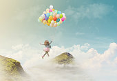 Little girl holding colorful balloons, jumping from one mountain top to the other; success/achievement concept, fantasy background with copy space