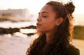 Shot of an attractive young woman sitting alone on a mat and meditating on the beach at sunset