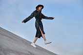 Beauty Fashion woman in black round hat and leather raincoat near lake pond. Portrait girl at sunset. Beautiful makeup and bright red lipstick on lips