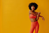 attractive young fit woman in sportswear stretching isolated on orange background