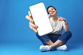 Happy woman shows blank smartphone screen against blue background