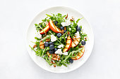 Peach, blueberry and arugula fresh fruit salad with cheese and almond nuts, top view