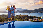 A family on summer holidays stands by the swimming pool and enjoys the beautiful sunset