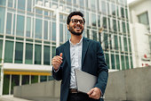 Smiling indian businessman in suit and glasses with laptop near office building