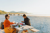 Woman and Man camping at the scenic beach and having picnic during Midnight Sun on Lofote Islands