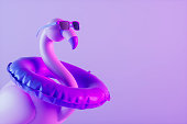 Inflatable flamingo with sunglasses and swim ring on neon purple background minimal summer travel holiday background