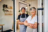 Coffee shop, senior woman manager portrait with barista feeling happy about shop success. Female server, waitress and small business owner together proud of cafe and bakery growth with a smile