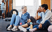 Gym, laughing and group of mature women telling joke after fitness class, conversation and comedy on floor. Exercise, bonding and happy senior woman with friends sitting chatting together at workout.