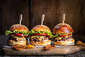 Tasty cheeseburger with lettuce, cheddar cheese, tomato and pickles. Burger bun with sesame seeds. Rustic atmosphere. Delicious fast food meal.