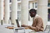 Side view of young African American businessman networking in street cafe