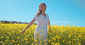 Relax, freedom and happy woman in field of flowers with blue sky, countryside and natural spring wellness. Nature, zen breathing and girl walking in floral grass with peace, smile and green plants.