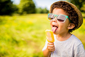 Boy in sunglasses and hat eating popsicle outdoors