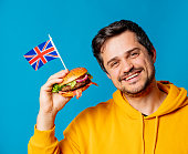 Smiling guy in yellow hoodie with burger and Uk flag on blue background