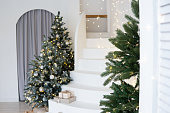 A large Christmas tree in the living room, decorated with garlands and light balloons. Bright Christmas interior with a white staircase.