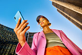 Young African American woman in colorful clothing using a smartphone. Low angle shot with concrete silos in the background. Urban fashion and technology concept.