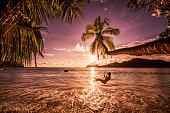 Carefree woman swinging above the sea at sunset beach.