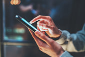 Closeup view of woman holding modern smartphone in hands.Girl typing on empty mobile screen. Horizontal, blurred background, bokeh effects.