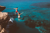 Young brave divers couple jumping off cliff into ocean