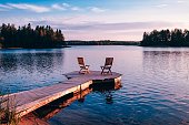 Two wooden chairs on a wood pier overlooking a lake at sunset