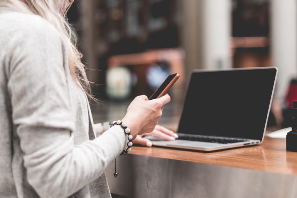 Woman Using Her Smartphone While Working Remotely on Laptop Free Photo